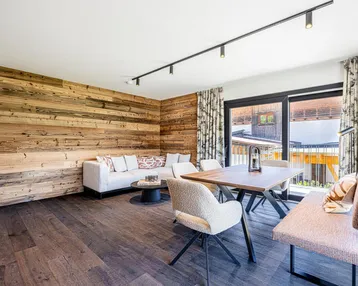 Gemütlicher Wohn-Essbereich mit Holzwand, bequemer Couch und Zugang zum Balkon durch große Fenster.