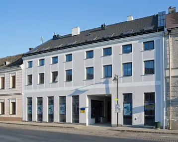 Mehrstöckiges Gebäude mit hellgrauer Fassade und vielen Fenstern an einer städtischen Straße.