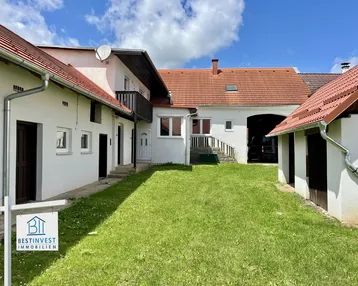 Blick auf den Innenhof der Immobilie mit mehreren Gebäuden und grünem Rasen unter blauem Himmel.