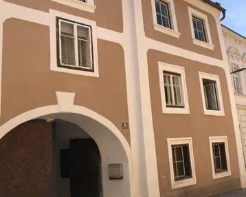 Historische Fassade eines Gebäudes mit braunem Putz und weißen Akzenten sowie einem großen Holztor.