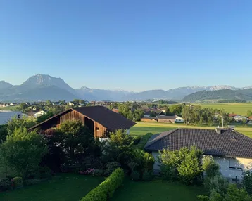Weitläufiger Blick über die ländliche Umgebung mit grünen Feldern und majestätischen Bergen im Hintergrund.