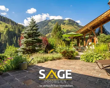 Geräumige Steinterrasse mit Liegestühlen, Sonnenschirm und weitem Blick auf die umliegende Berglandschaft.