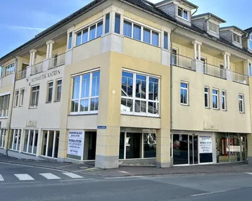 Gebäude mit gelber Fassade und großen Fenstern an einer Straßenecke, mit Gewerbeflächen im Erdgeschoss.