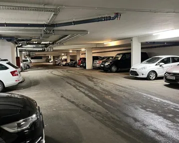 Geräumige Tiefgarage mit zahlreichen Stellplätzen und sichtbaren Installationen an der Decke.
