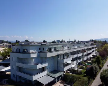 Luftaufnahme eines modernen Mehrfamilienhauses mit mehreren Balkonen, Dachterrassen und Carports.
