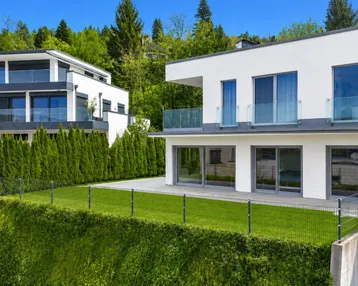 Moderne Neubauten mit weißer Fassade, großen Fensterfronten und gepflegtem Rasenbereich.