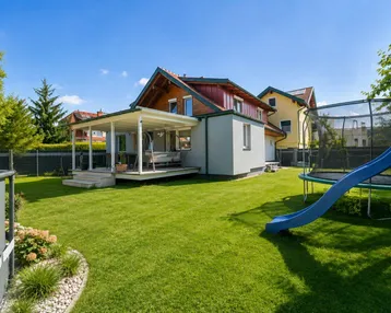 Großer Garten mit Rasenfläche, überdachter Terrasse und Spielgeräten für Kinder.