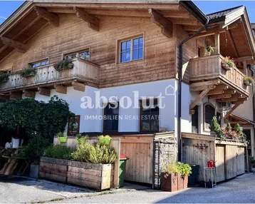 Traditionelles Holzhaus mit weißer Fassade und Balkonen in alpiner Umgebung.