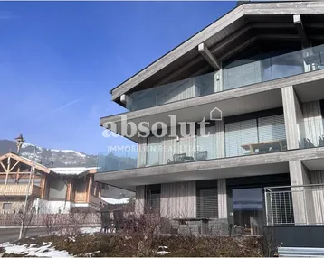 Modernes Gebäude im alpinen Stil mit Holzelementen, Glasbalkonen und verschneiter Umgebung.