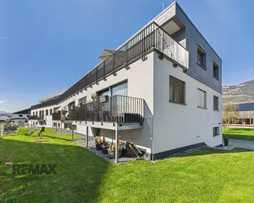 Modernes Mehrfamilienhaus mit Balkonen und gepflegter Rasenfläche in sonniger Lage.