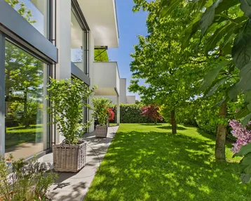 Gepflegter Gartenbereich mit Rasenfläche und modernen Pflanzkübeln neben der Hausfassade.