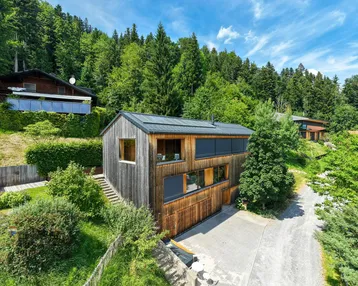 Modernes Holzhaus in Hanglage, umgeben von grünen Wäldern und Natur.