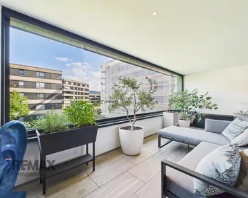 Heller, verglaster Balkon mit bequemen Loungemöbeln und Blick auf die Umgebung.
