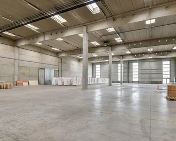 Große, leere Lagerhalle mit hohen Decken, Betonwänden und Oberlichtern, bereit zur Nutzung.