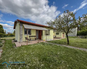 Kleines Einfamilienhaus mit gelber Fassade und Vorgarten unter blauem Himmel.