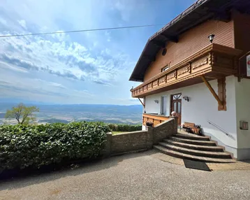 Traditionelles Gebäude mit Holzbalkonen und weitem Blick über die Landschaft unter blauem Himmel.