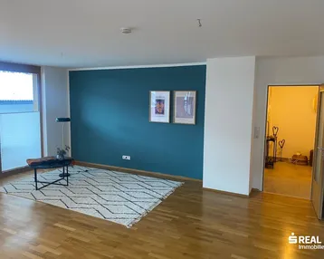 Helles Wohnzimmer mit Holzboden, einer blauen Akzentwand und großem Fenster.