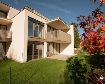 Moderne Fassade mit Balkon und großzügiger Rasenfläche, umgeben von Herbstlaub.