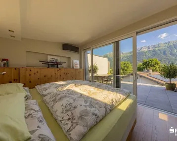 Helles Schlafzimmer mit Holzboden, großen Glasfronten und Zugang zu einer Terrasse mit Bergblick.