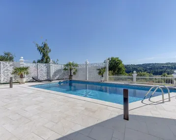 Großer Außenpool mit gefliestem Becken und umliegender Terrasse, umgeben von einer dekorativen Mauer.