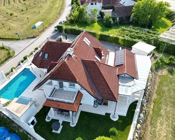 Luftaufnahme eines luxuriösen Hauses mit Pool, Terrasse und Solaranlagen auf dem Dach.