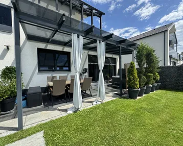Überdachte Terrasse mit Esstisch und Stühlen, umgeben von einem gepflegten Rasenbereich.