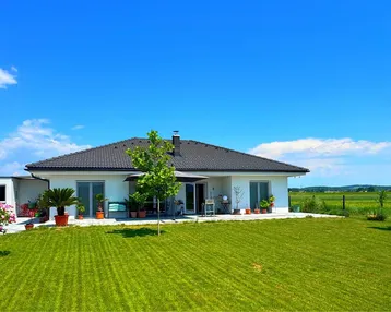Modernes Einfamilienhaus mit großem Garten und weitem Blick ins Grüne unter blauem Himmel.
