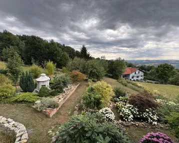 Weitläufiger, gepflegter Garten mit vielfältiger Bepflanzung, Steinmauer und Fernblick auf die Landschaft.
