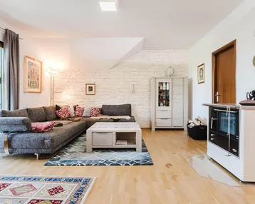 Helles Wohnzimmer mit Holzboden, gemütlichem Sofa und modernem Kaminofen.