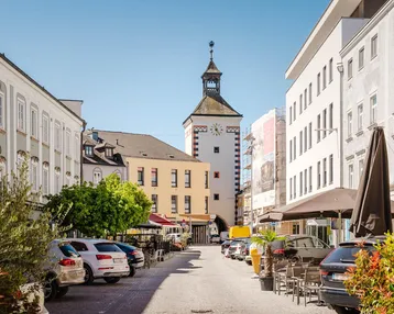 Malerische Gasse mit historischen Gebäuden und einem Uhrturm unter blauem Himmel.