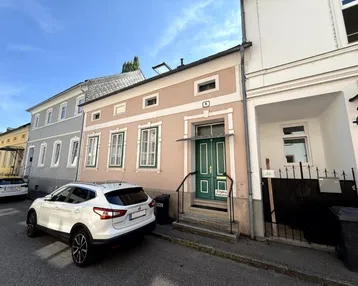 Fassade eines Wohnhauses von der Straße aus gesehen mit einem geparkten Auto davor.