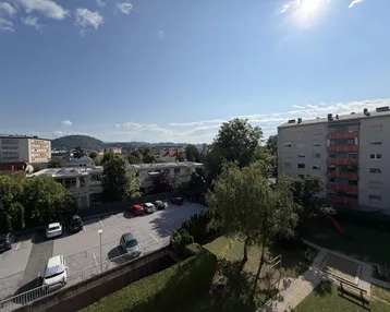 Blick über einen Parkplatz und Wohngebäude in einer städtischen Umgebung unter blauem Himmel.