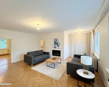 Helles Wohnzimmer mit Fischgrätparkett, modernen Sofas und einem dekorativen Kamin.