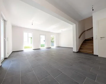 Geräumiges, helles Wohnzimmer mit modernem Fliesenboden und Zugang zum Gartenbereich.