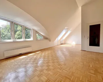 Helles Dachgeschosszimmer mit Parkettboden, schrägen Wänden und mehreren Fenstern, die viel Tageslicht hereinlassen.