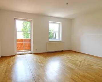 Helles Zimmer mit Parkettboden und Zugang zu einem kleinen Balkon, ideal als Wohn- oder Schlafzimmer.
