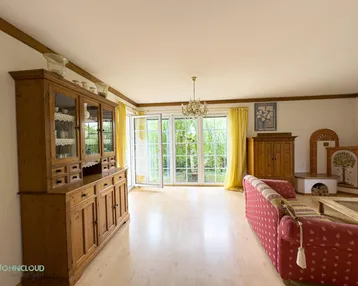 Geräumiges Wohnzimmer mit traditionellen Holzmöbeln, Kamin und Zugang zum Garten.
