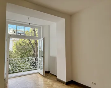 Helles Zimmer mit Fischgrätparkett und einem französischen Balkon mit schmiedeeisernem Geländer.