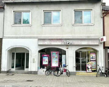Gebäude mit Geschäftsfassade im Erdgeschoss und Wohnungen darüber, mit Fahrrädern davor auf der Straße.