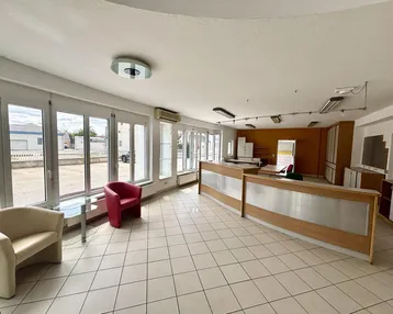 Empfangsbereich oder Verkaufsraum mit Fliesenboden, Sitzgelegenheiten und großen Fenstern.