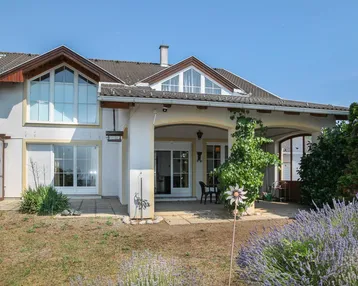 Hausfassade mit überdachter Terrasse, Sitzbereich und blühendem Lavendel im Vorgarten.