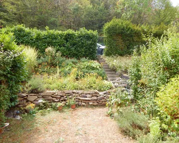 Gestufter Garten mit Natursteinmauern, üppiger Bepflanzung und Treppenaufgang, umgeben von Grün.