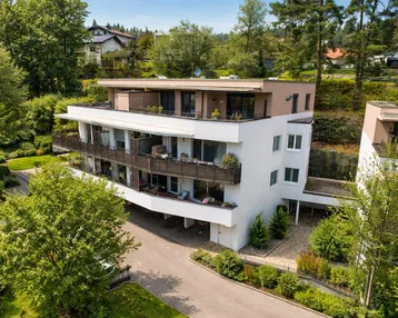 Moderne Wohnanlage mit mehreren Balkonen und Dachterrasse, eingebettet in eine grüne Umgebung.