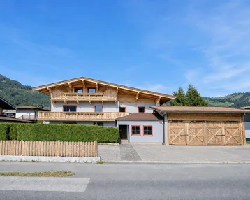 Traditionelles Haus mit Holzverkleidung und Doppelgarage in alpiner Umgebung unter blauem Himmel.