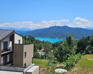 Modernes Gebäude mit Satteldach und weitem Blick auf den See und die umliegenden Berge.