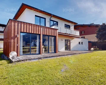 Modernes Wohnhaus mit Holzfassade, großer Holzterrasse und gepflegtem Rasenbereich.