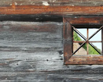 Alte, verwitterte Holzwand mit einem kleinen, rustikalen Fenster und Blick ins Grüne.