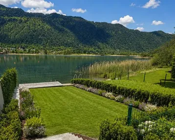 Gepflegter Gartenbereich mit direktem Seezugang und Bergblick unter blauem Himmel.