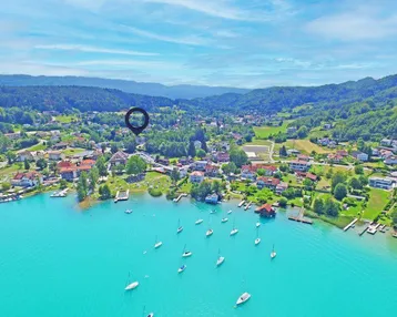 Luftaufnahme einer malerischen Seenlandschaft mit einem Dorf am Ufer, umgeben von grünen Hügeln und Bergen.
