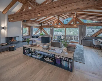 Geräumiges Wohnzimmer mit hohen Decken, freiliegenden Holzbalken und Kamin, bietet einen weiten Ausblick.